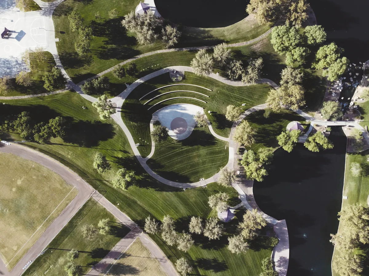 Aerial view of landscaped park with amphitheater, curved paths, and lake