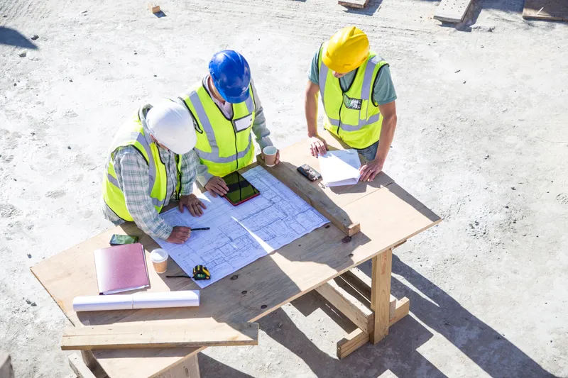 Workers in hi-vis reviewing blueprints on a wooden table